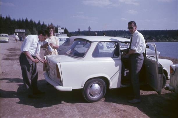 A photo of young friends standing by car. Men and woman are on road trip. They are in casuals on sunny day.