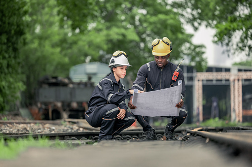 Locomotive engineers collaborating and referencing blueprint to guide maintenance task, troubleshoot issues within rial infrastructure and network. Ensuring reliability and safety of train operations