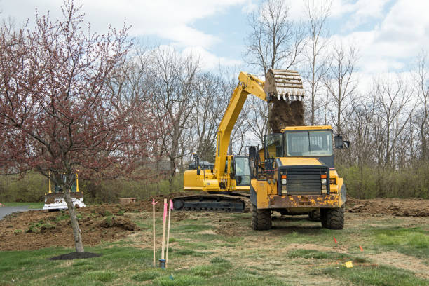 Backhoe loading excavated soil into dump truck bed in preparation for new building construction.