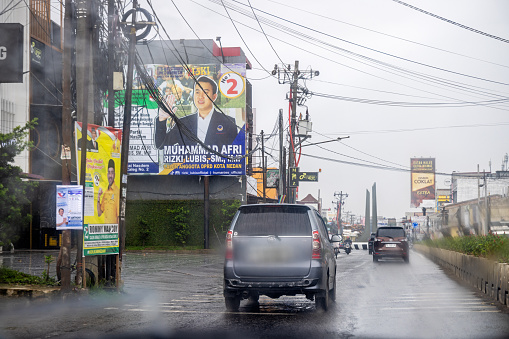 Medan, Sumatra, Indonesia - January 18th 2024:   Traffic on a rainy day with billboard posters in a suburb to Medan, the main city on North Sumatra