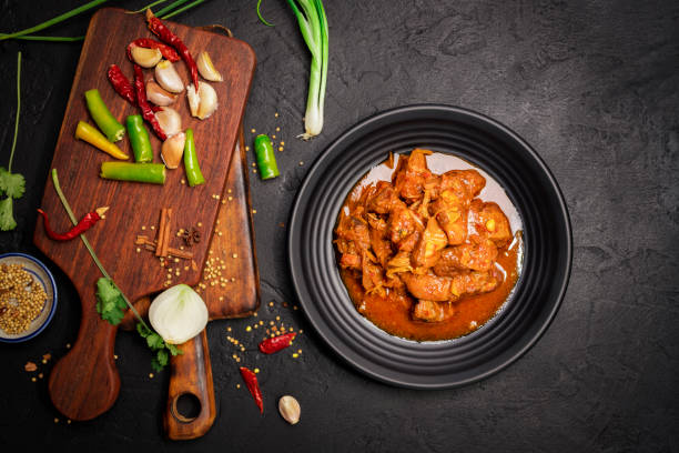 istock Delicious beef or pork stew in a rustic black plate with fresh coriander, red chilies, garlic, onions and spices placed on a black background, top view 2130234437