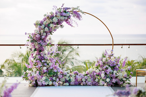 At the wedding ceremony facing the beautiful sea, a wedding arch adorned with white and purple flowers creates a picturesque scene.