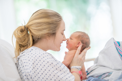 Young asian mother feeding breast her baby on bed at home in white room. Asia mom holding her baby and looking to her child.  Woman and new born relax in a white bedroom.