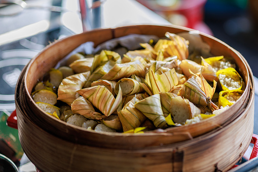 A stack of ketupat rice cakes is arranged in a large bamboo steamer, showcasing traditional Malaysian food.