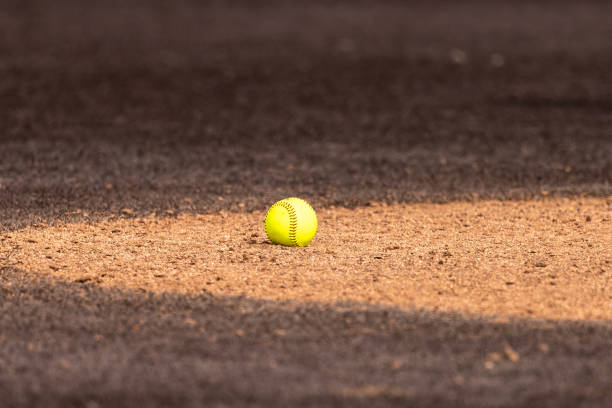 Optic yellow softball on clay pitchers circle with brown synthetic turf