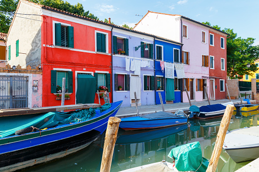 Разноцветные красочные дома в Венеции на острове Бурано. Узкий канал с моторными лодками вдоль домов. Летний солнечный день. Выборочная фокусировка.