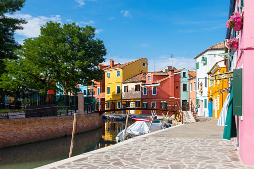 Разноцветные красочные дома в Венеции на острове Бурано. Узкий канал с моторными лодками вдоль домов. Летний солнечный день. Выборочная фокусировка.