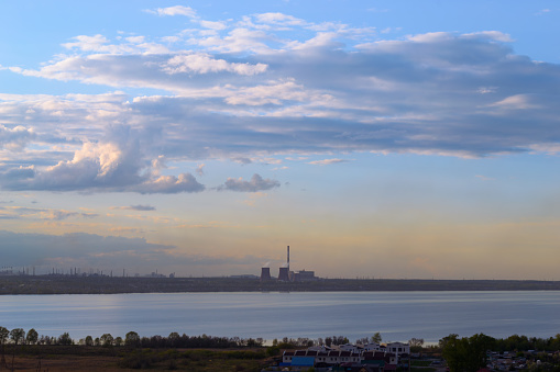 Thermal power plants and other factories stand on the shore of the lake at dusk at sunset