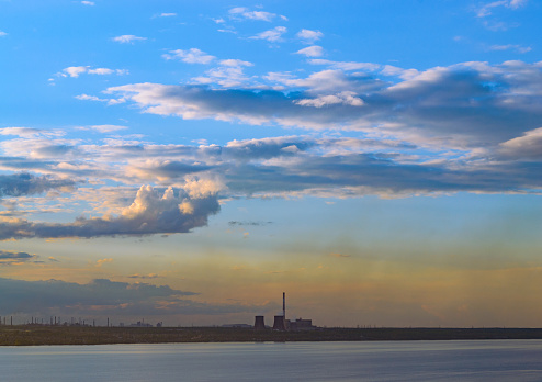 Thermal power plants and other factories stand on the shore of the lake at dusk at sunset
