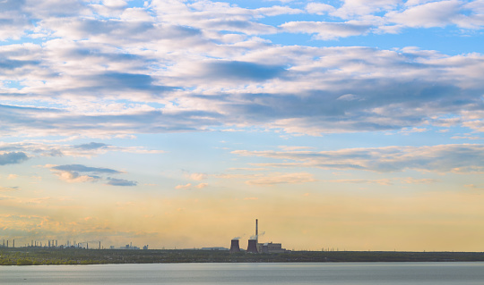 Thermal power plants and other factories stand on the shore of the lake under the evening sky