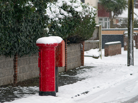 Red postbox crowned with snow on a winter day in England