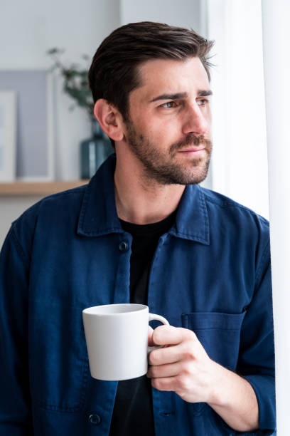 istock Thoughtful man holding coffee mug by window 2130376625