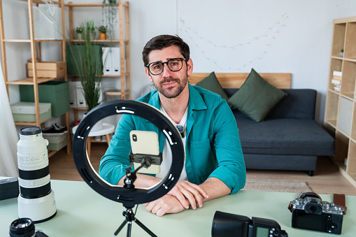 Young man smiles in a home studio setup with photography equipment and ring light