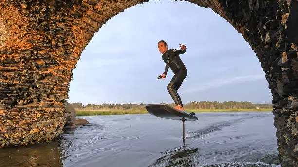 Hydrofoil rider gliding over the water with his board in one of the canals of the Ria de Aveiro in Portugal during sunset.