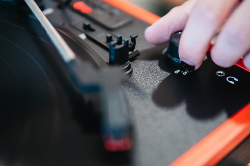Close-up of a finger adjusting the volume knob on a red portable vinyl turntable
