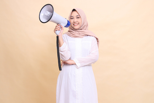 woman muslim asian in hijab looking at the camera smiling cheerfully holding a loudspeaker megaphone. Technology, broadcast and promotion concept