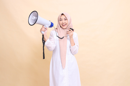 woman indonesia mature wearing a hijab into a camera smiling happily holding a loudspeaker megaphone and holding the speaker mic. Technology, broadcast and promotion concept