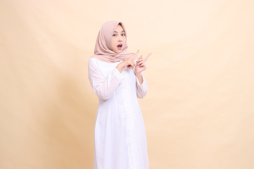 young woman indonesia muslim standing shocked both hands pointing to the top left. Fashion, pointer, business and promotion concept