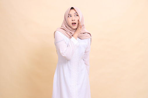 woman asian muslim standing to camera hands near mouth shouting gracefully giving candid important announcement. Fashion, pointer, business and promotion concept