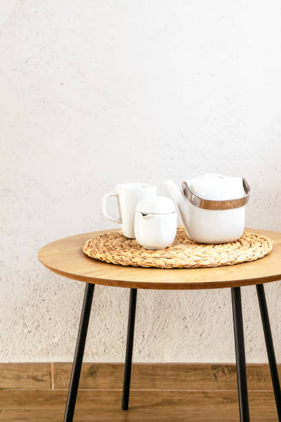 istock Wooden table with ceramic tea or coffee pottery set against white wall. Vertical with copy space. 2130517665