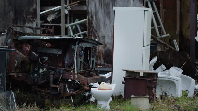 Dead engine, abandoned fridge, toilet and other trash outside with grass around, handheld