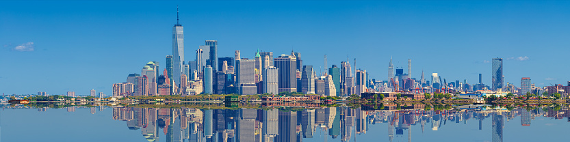 New York City Skyline with Battery Park, World Trade Center, Empire State Building, Chrysler Building, Manhattan Financial District, Governors Island, Red Hook neighborhood of Brooklyn and Clear Blue Sky all reflected in Water of New York Harbor. High Resolution Stitched Panoramic image with 4:1 image aspect ratio. Canon EOS 6D Full Frame Sensor Camera and Canon EF 70-200mm f/4L IS USM Lens.