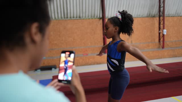 Gymnast girl being filmed on the mobile phone walking on the balance beam in a gymnasium