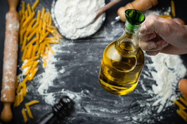 Hand holding olive oil over preparation bread, pasta, pizza background.