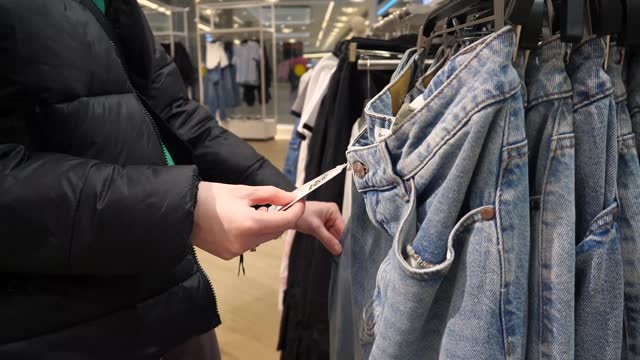 A woman chooses jeans in a clothing store and reads the label.