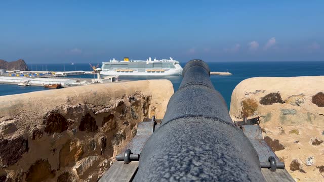 A canon over the Gulf of Oman at Muttrah Fort with a cruise ship in the port