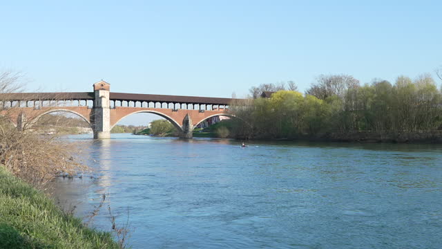 Nice view of Ponte Coperto (covered bridge) is a bridge over the Ticino river in Pavia at sunny day, man sailing on a canoe, Lombardy, Pavia, Italy