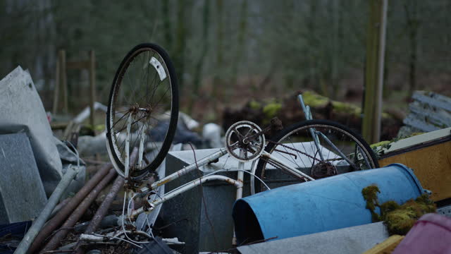 Broken bike on pile of trash with forest behind, outside, handheld.