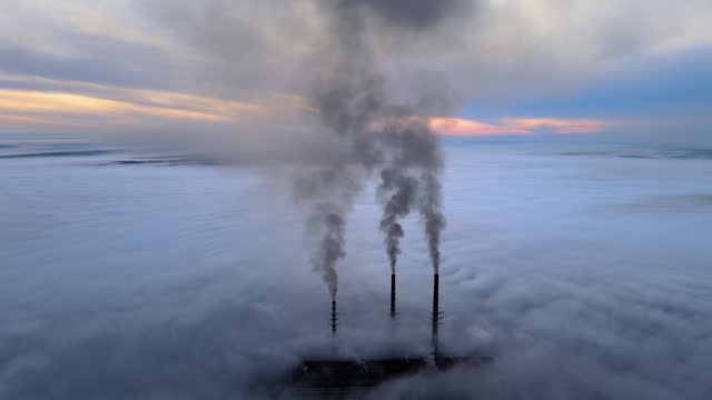 Aerial view of coal power plant high pipes with black smoke moving up polluting atmosphere at sunset
