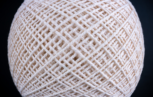 A close up of a white ball made of yarn. The yarn is woven in a pattern, creating a textured surface. The ball appears to be a small, round object, possibly a toy or decorative piece