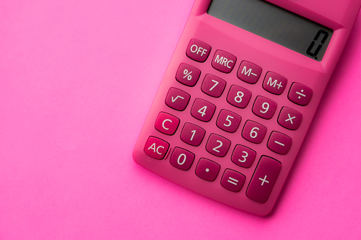 High angle view and close up of a pink modern calculator with white numbers on a pink surface