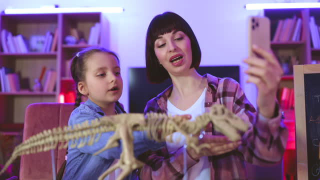 Happy mother examine skeleton of dinosaur with smart cute daughter.