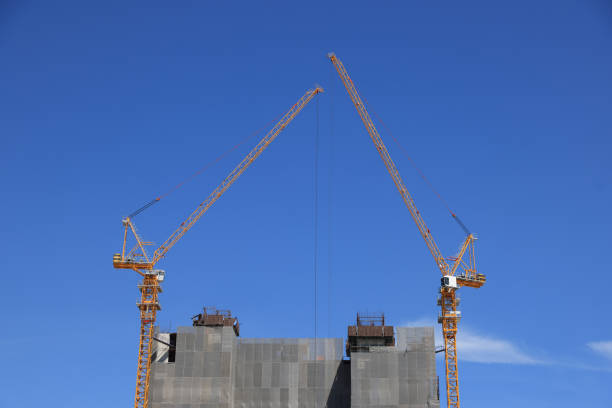 Two construction cranes are positioned on top of a newly constructed building, symbolizing business investment.