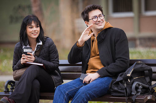 Male and female student drinking coffee together on a park bench