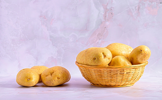 Fresh Potatoes in Wicker Basket on Light Marble Surface