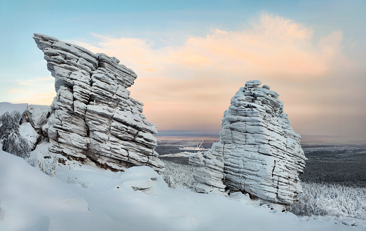 Mystical dawn in the snow-covered mountains. Rock pillars, weathering posts. High stone cliff covered with snow and rise above the coniferous forest at sunset. Perm region.