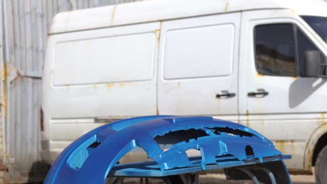 man spray paints a car bumper blue