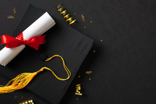istock Graduation cap with diploma on black background. Flat lay, top view. 2130878992