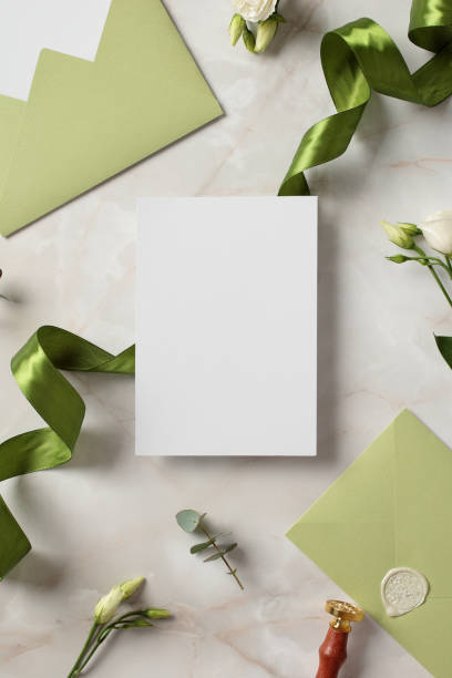 istock Blank wedding invitations card mockup with space for text, green ribbon, olive envelopes, flowers on stone background. 2130882705