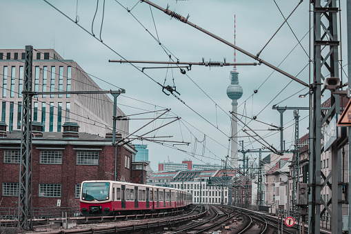 Suburban or Sbahn train of Berlin is approaching Friedrichstrasse station. Public transport in Berlin, visible typical houses and landmark as TV tower on Alexanderplatz in the background.. Cold spring day