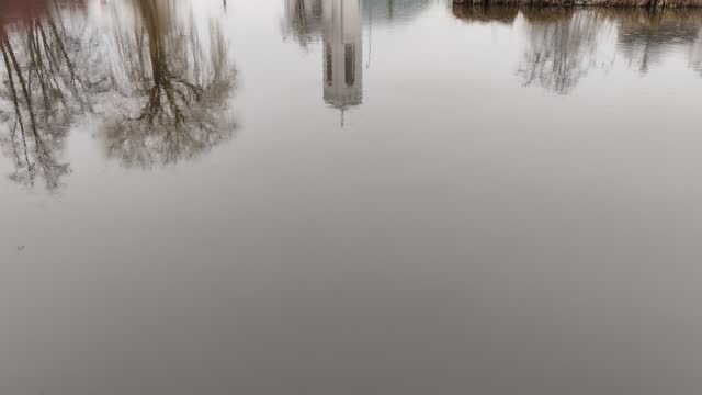 Trees and a church are reflected on the surface of the pond in rainy weather.