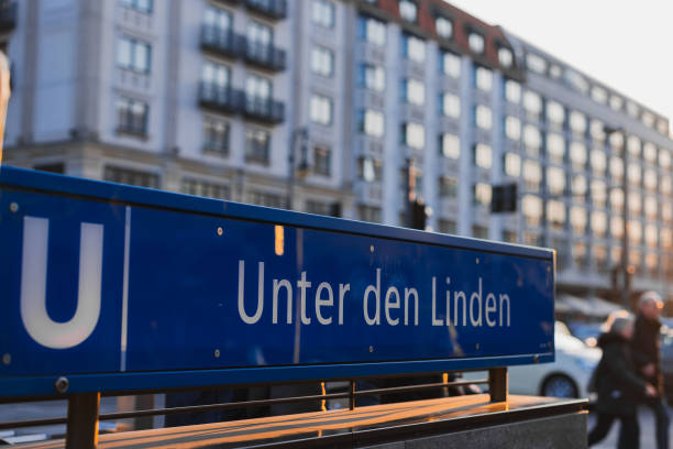istock Evening setting at the display board for Unten den Linden underground station in Berlin. Some people seen walking past, beautiful sunlit buildings seen in the background 2130892122