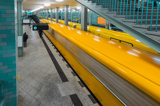 Metro or ubahn station of Alexanderplatz in Berlin. Underground station as part of berliner metro system. Green vintage tiles and yellow train in motion blur racing past the camera.