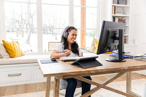 Working from her office at home, the mid adult female freelancer smiles at her client during a video conference.