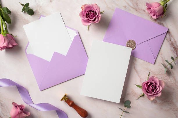 istock Blank white paper card, violet envelopes, roses on marble background. Flat lay, top view, copy space. Wedding invitation card design. 2130893741