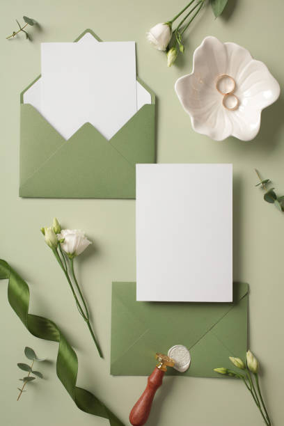 istock Wedding flat lay composition with invitation card mockup, green envelopes, flowers on pastel green background. Top view with copy space. 2130907334
